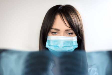 The topic of coronavirus and safety. Young female doctor in a surgical suit on a light background...
