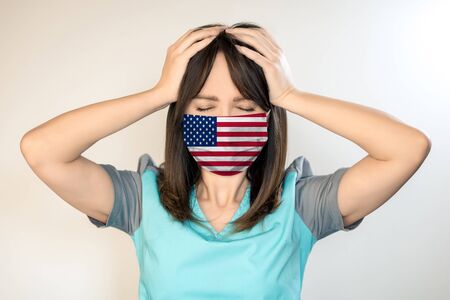 Theme of health and safety. A young female doctor with dark hair in a mask from a virus with the US flag, holds on his head.の写真素材