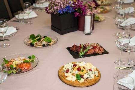 several trays of assorted cheeses with strawberries and cold cuts with herbs.
