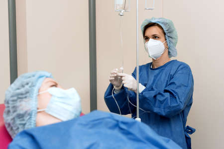 doctor girl in a mask, gown and gloves sets up a drip