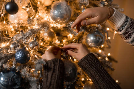 close-up of the hands of a man and a woman decorate the Christmas tree with ballsの写真素材