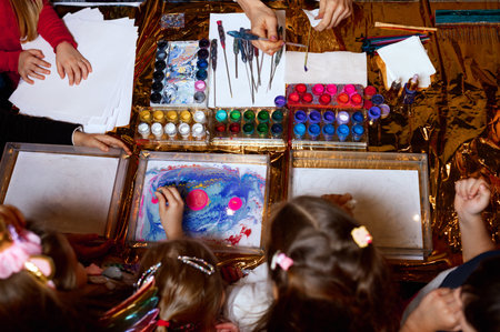 happy children. Top view creative photo of little boys and girls on the table drawing together with paints on paperの写真素材