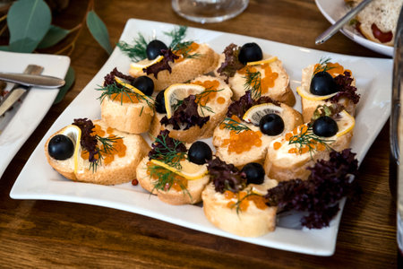a lot of sandwiches with caviar, olives and lemon on a white plateの写真素材