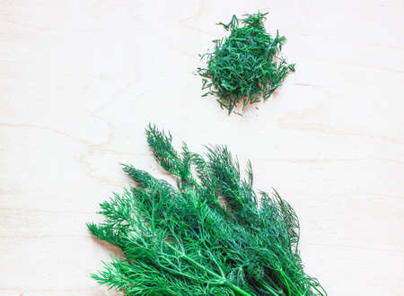 Bunch of dill on a wooden board. Next to a handful of chopped dill.の写真素材
