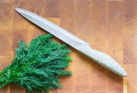 Bunch of dill on a wooden board. Next to the kitchen knife.の写真素材