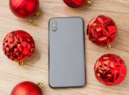 A popular smartphone with Christmas balls. The smartphone rests on a wooden surface on the screen next to the Christmas balls.の写真素材
