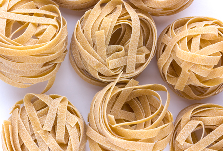 Macaroni nest close-up on a white surface. Tagliatelle macaroni lie a bunch next to each other.の写真素材