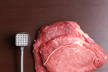 Fresh beef steak on the table. Raw pieces of marbled beef and hammer for beating close-up on the table.の写真素材