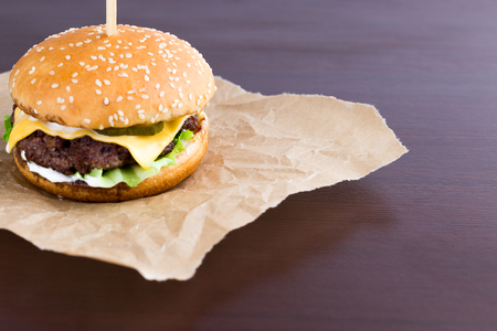 Burger on parchment paper. Beef patty burger, cheddar cheese, lettuce, bacon, tomato and balsamic sauce.の写真素材