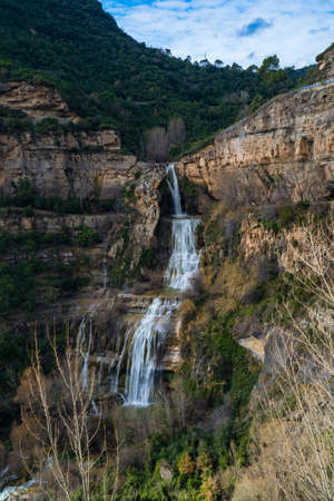 big waterfall falling down yellow rock cliff in the middle of the forest, sant miquel del fai catalonia, spainの写真素材