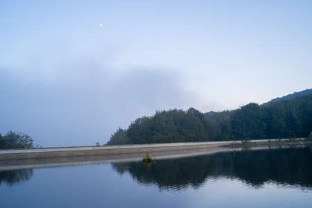 reservoir of  Santa Fe del Montseny at dusk with partially cloudy background, moon in the background and reflection in the water, Catalonia, Spainの写真素材