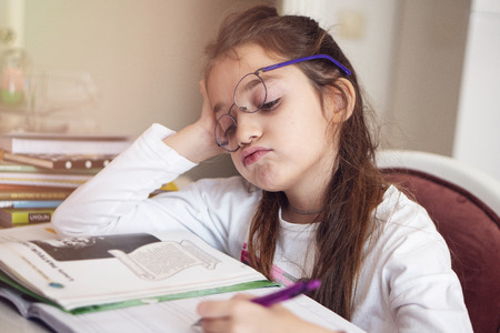 Bored little girl at home. Cute child doing homework. Modern education, communication