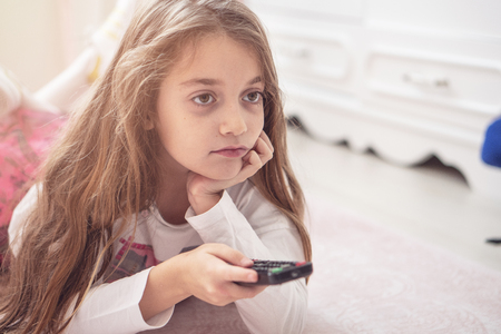 Cute little girl with a tv remote at homeの写真素材