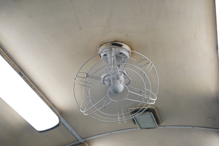 A close-up of a vintage electric fan on the ceiling of an old train car.の写真素材