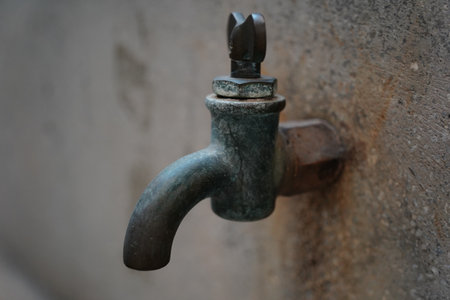 Close-up of an old, weathered brass water tap on a concrete wall.