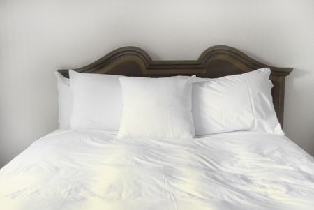 Group of several white pillows on a bed with headboardの写真素材