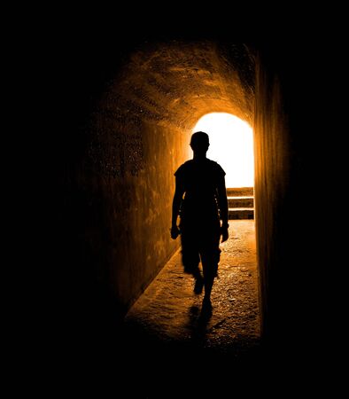 Person in long tunnel walkway with white light at the endの写真素材