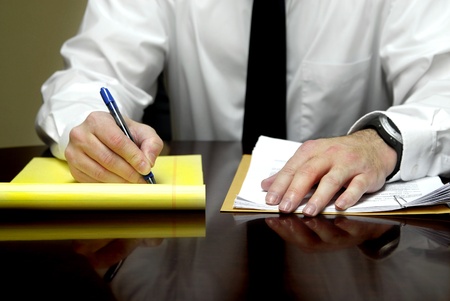 Business man sitting at desk holding pen with files
