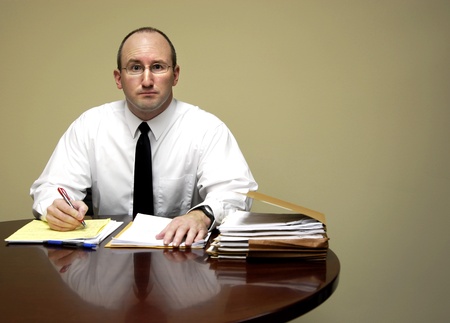 Business man sitting at desk holding pen with filesの写真素材