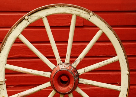Old weathered wagon wheel leaning against red wall の写真素材