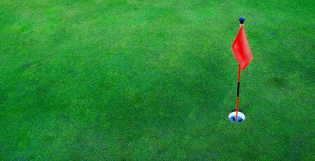 Red flag and hole for golf on green grassの写真素材