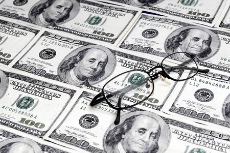 Several one hundred dollar bills with black glasses on topの写真素材