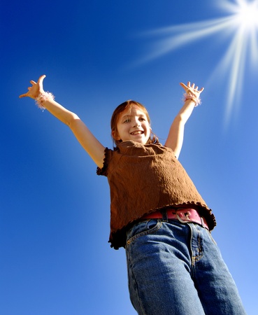 Young joyful girl with arms raised up towards perfect blue sky and sunshineの写真素材