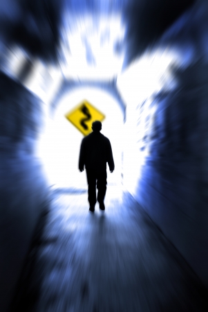 Person in long tunnel walkway with white light at the end and a sign showing curves aheadの写真素材