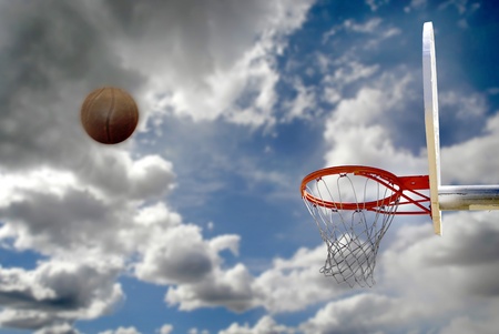 Outdoor basketball with clouds and sky and shot to the hoop