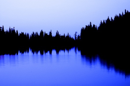 Silhouette of forrest reflecting in mountain lakeの写真素材