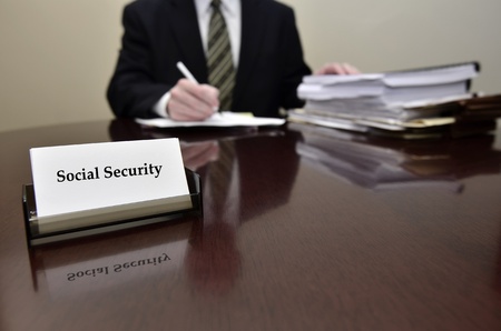 Man sitting at desk holding pen papers with business card for Social Securityの写真素材