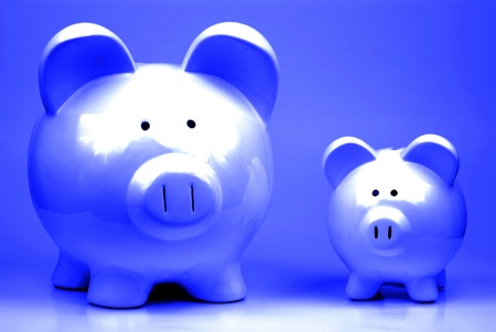 Two white piggy banks standing on blue background symbolizing savings adn moneyの写真素材
