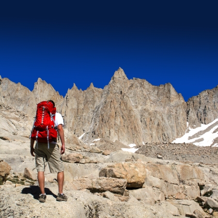 Man standing on rough rock hiking a tall mountain with blue sky                    の写真素材