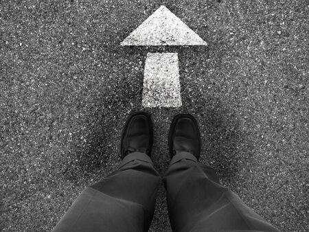 Business man standing on ground with arrow pointing the direction to goの写真素材