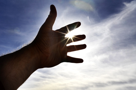 Persons hand reaching in hope towards heaven with sunlight shining throughの写真素材