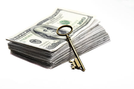Old key laying on top of stack of cash moneyの写真素材