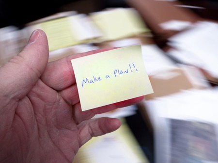 Messy office with hand holding note saying Make a Planの写真素材