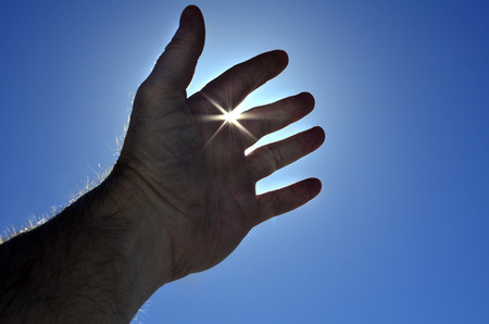 Persons hand reaching in hope towards heaven with sunlight shining throughの写真素材