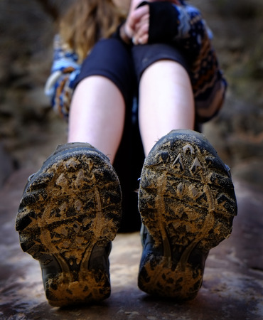 Young girl wearing hiking boots muddy sitting on rockの写真素材