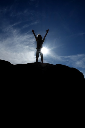 Silhouette of hiker at the top of a peak with blue sky in backgroundの写真素材