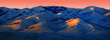 Snow capped mountain range in winter with sunrise or sunset light pink orange