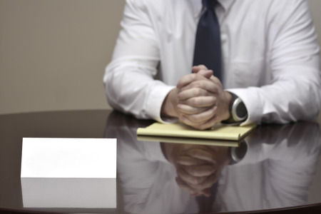 Businessman at desk with papers and card making hand gesturesの写真素材