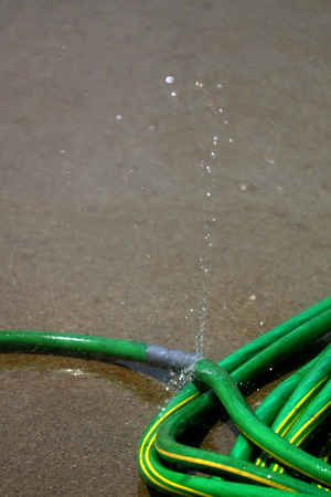 Green hose leaking and spraying water aroundの写真素材
