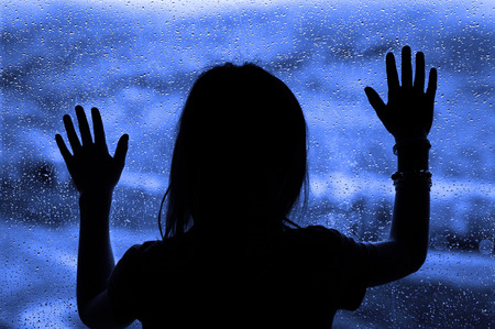 Rainy Day with little girl at window looking out wanting to playの写真素材