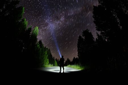 Man standing in dark with stars with flashlight forest night skyの写真素材