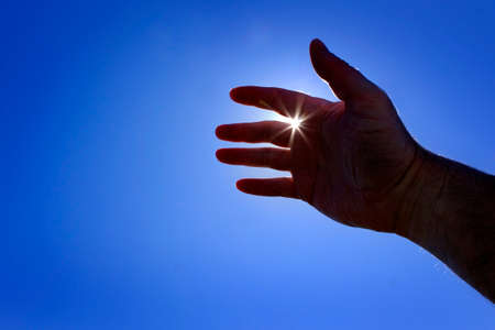 Hand reaching up towards heaven seeking help with sunstar sunshine inspiration guidanceの写真素材