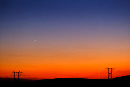 Sunset and Moon in sky in landscape with power lines on horizon