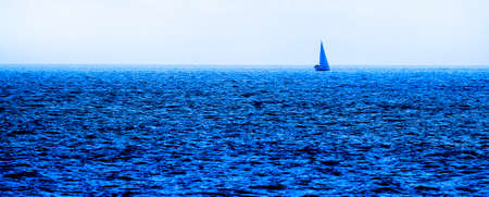Single sailboat alone out on blue ocean