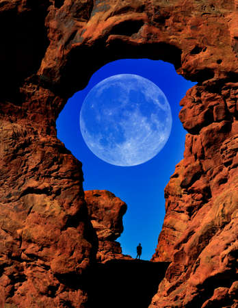 Silhouette of hiker in arch canyon rock formations with full moon in sky