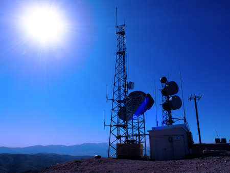 Radio towers for telecommunications and transmissions with blue sky and sun